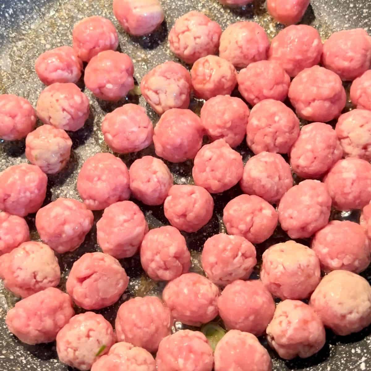 A large pan filled with meatballs made from ground pork getting ready to get cooked.