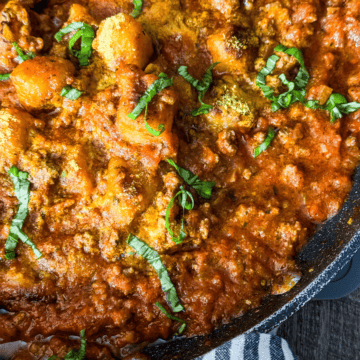 A pan filled with gnocchi bolognese garnished with fresh basil, ready to be served.