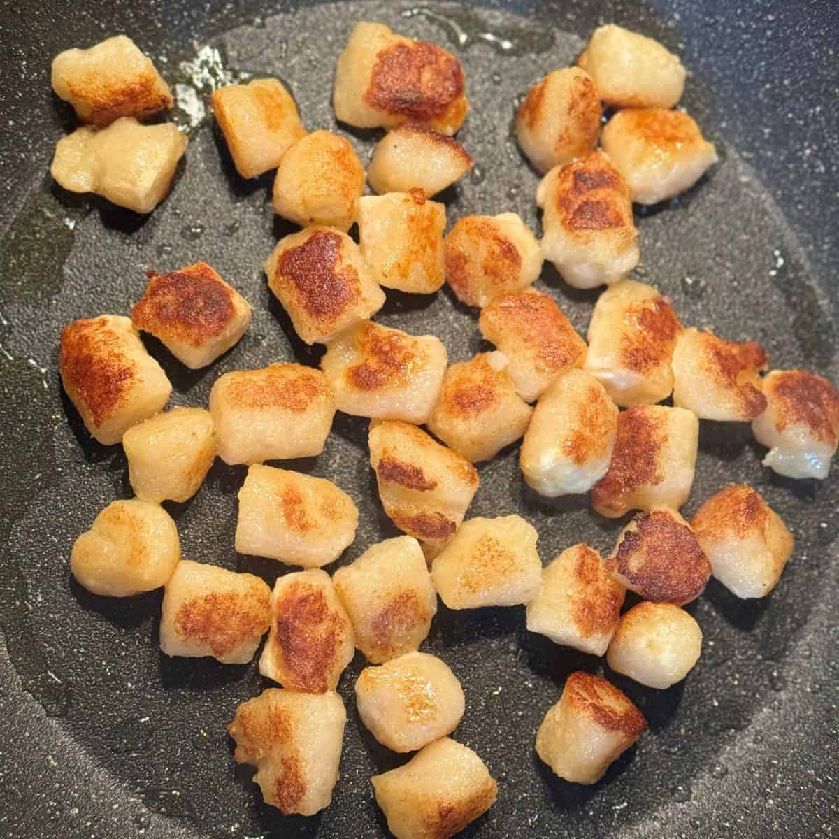 Cauliflower gnocchi being sautéed in a pan to achieve a golden color and crispy texture.