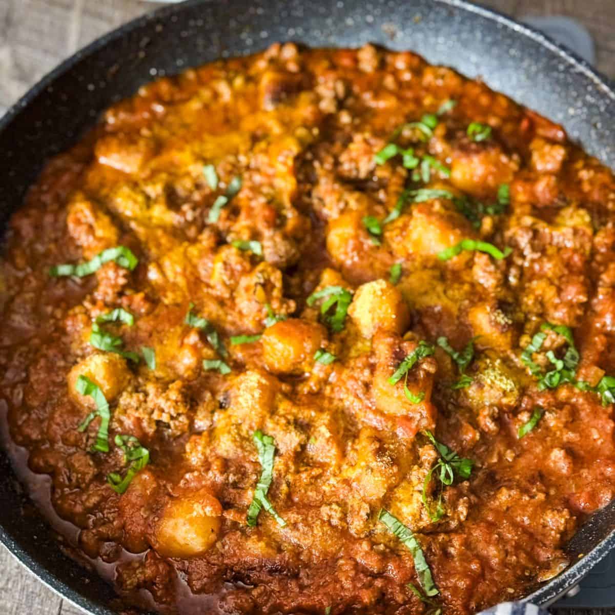 A pan filled with gnocchi bolognese garnished with fresh basil, ready to be served.