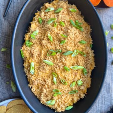 A black oven-safe baking dish with buffalo chicken dip spread evenly garnished with scallions and pork panko ready to be enjoyed.