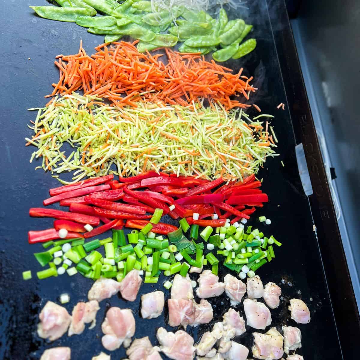 Chopped vegetables and chicken on a blackstone grill top.